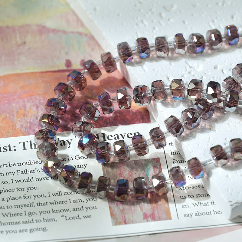 Faceted round beads in smoky purple glass with an iridescent finish arranged in loops on a printed magazine page