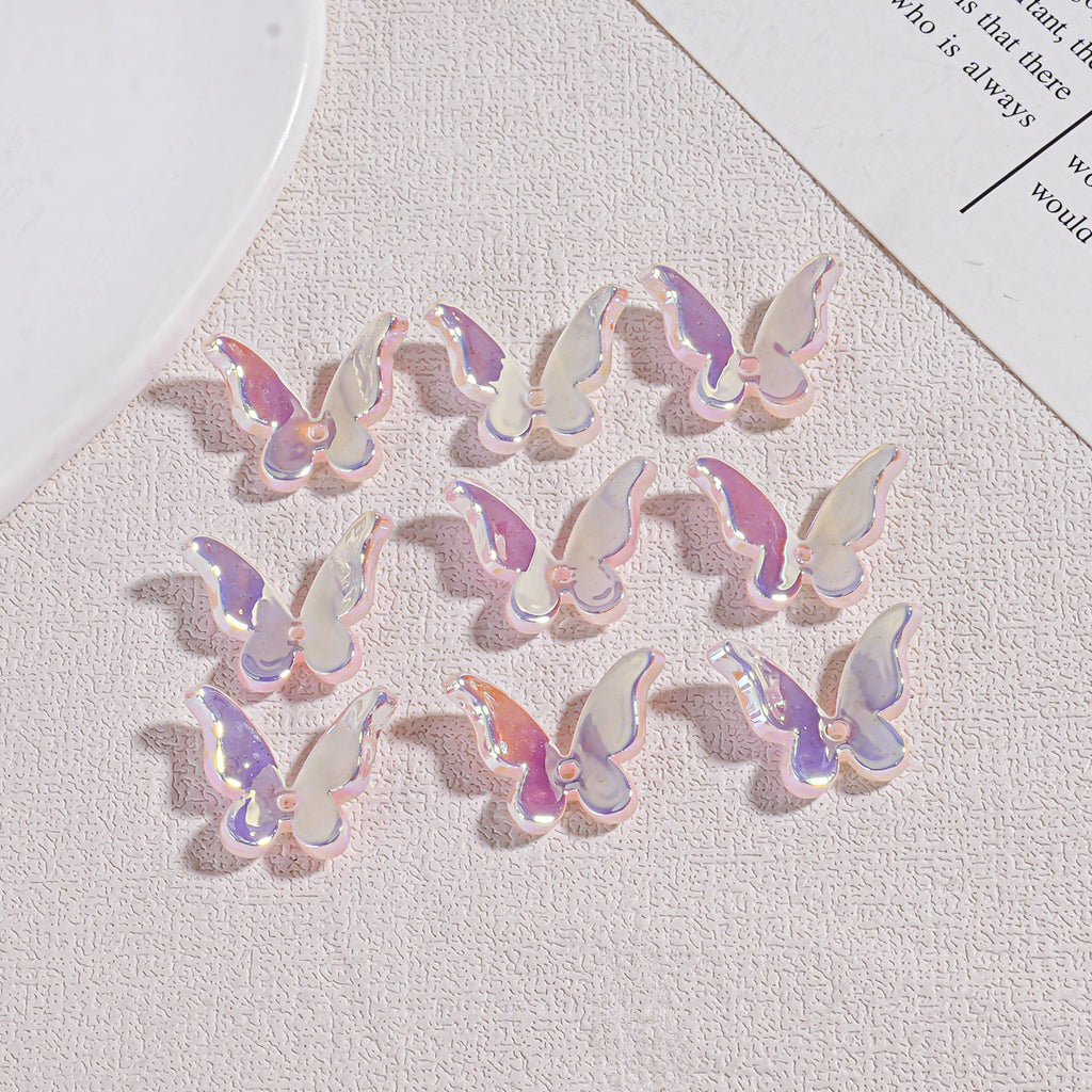 Twelve iridescent butterfly acrylic beads on textured beige surface with plate and paper