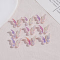 Twelve iridescent butterfly acrylic beads on textured beige surface with plate and paper