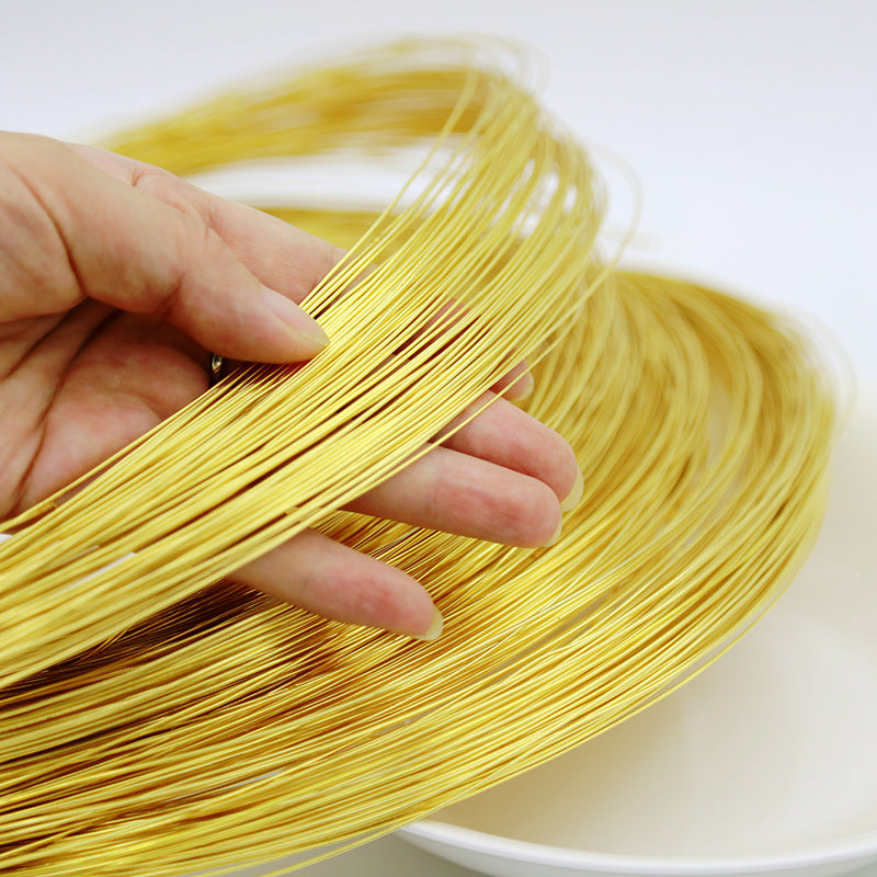A hand holding a bundle of thin, shiny gold-colored wire strands over a white surface.