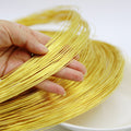 A hand holding a bundle of thin, shiny gold-colored wire strands over a white surface.