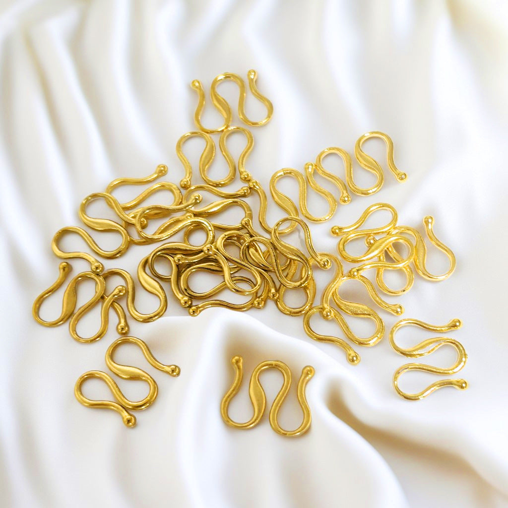 A pile of gold-colored, S-shaped metal hooks or clips scattered on a draped white fabric background.