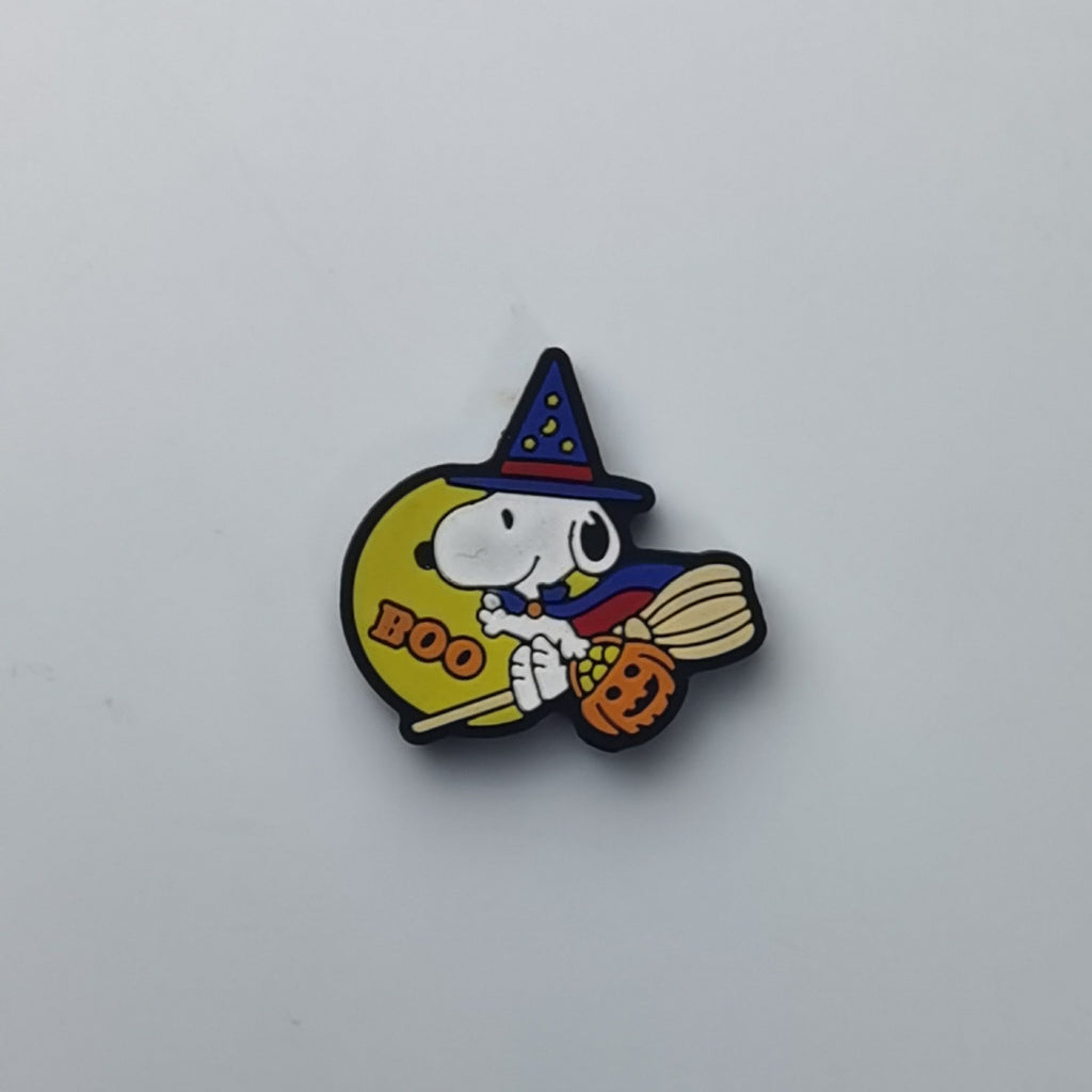 A small Halloween-themed enamel pin featuring Snoopy riding a broomstick on a yellow moon with 'BOO' text, a witch hat, and a pumpkin, shown on a plain light gray background.