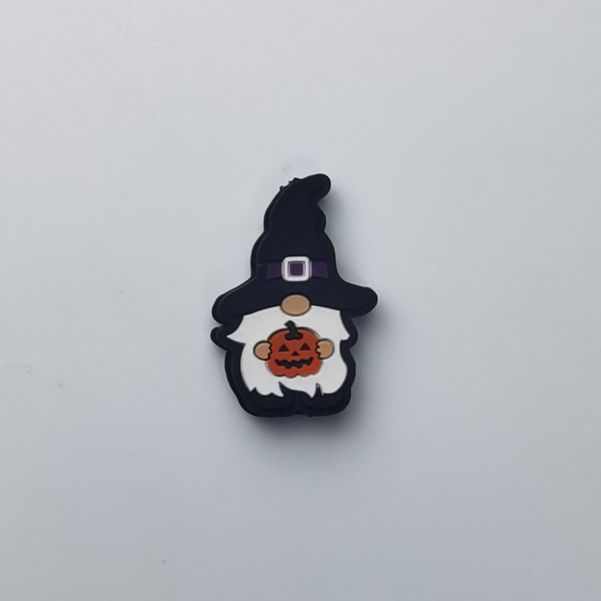 A small Halloween gnome charm or pin featuring a black witch hat, white beard, and a jack-o'-lantern pumpkin, shown on a plain light gray background.
