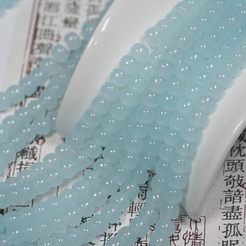 Light blue translucent round beads draped over a white ceramic spoon and printed book pages.