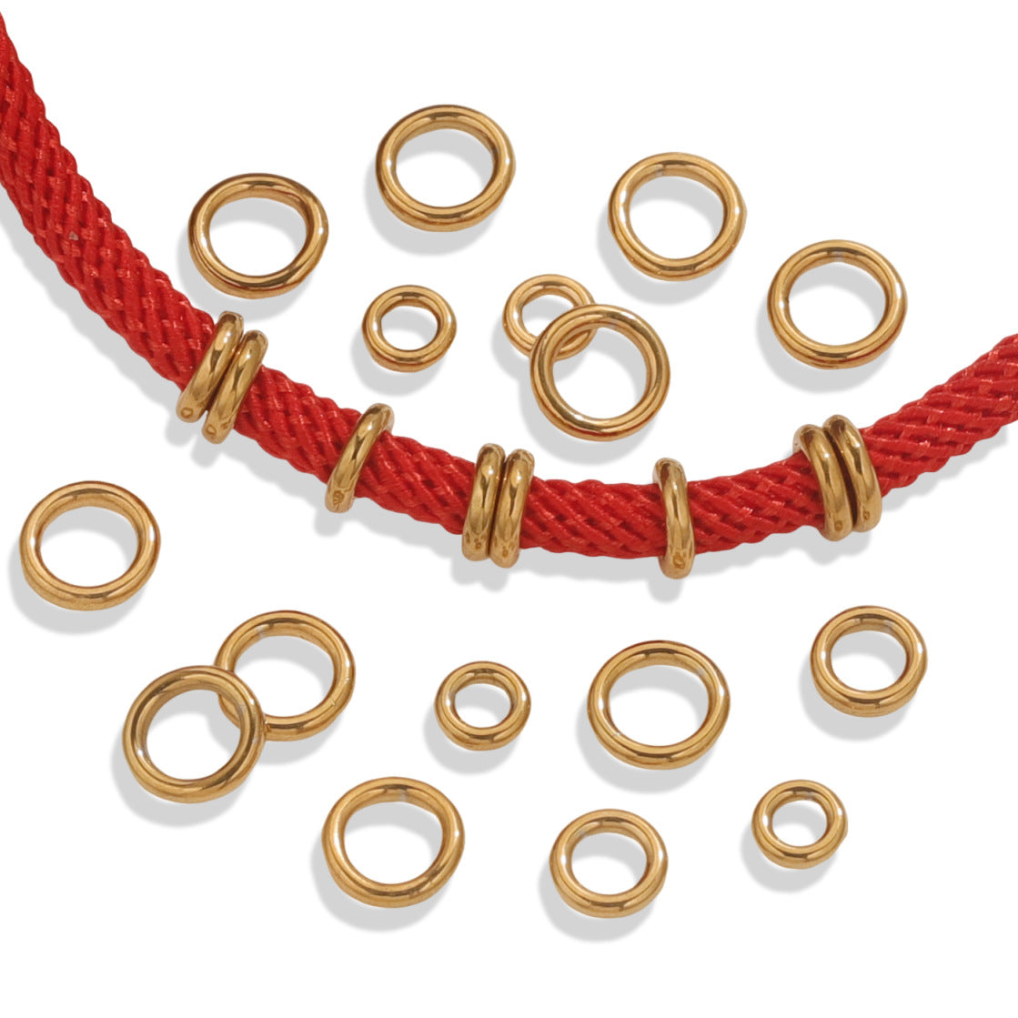 Gold-tone closed jump rings scattered on a white background with a red braided cord threaded through several rings