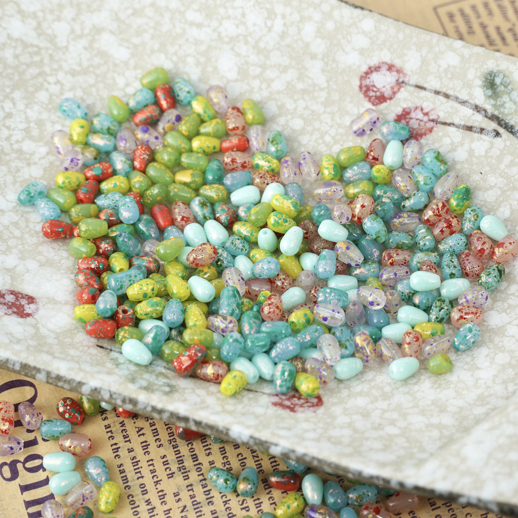 Colorful speckled glass teardrop beads on a white heart-shaped dish over a book page