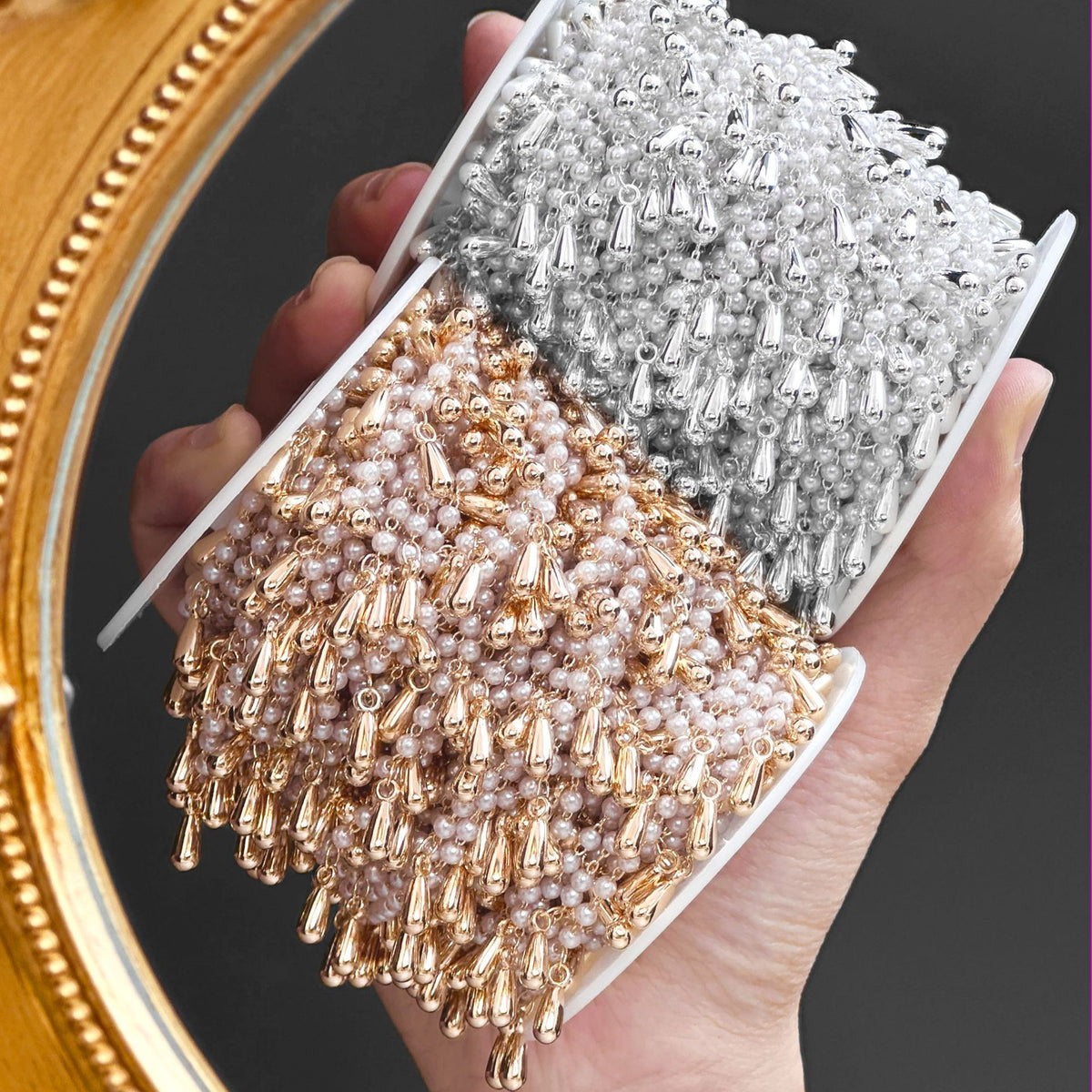 Hand holding display tray of silver and rose gold beaded fringe chains with teardrop drops