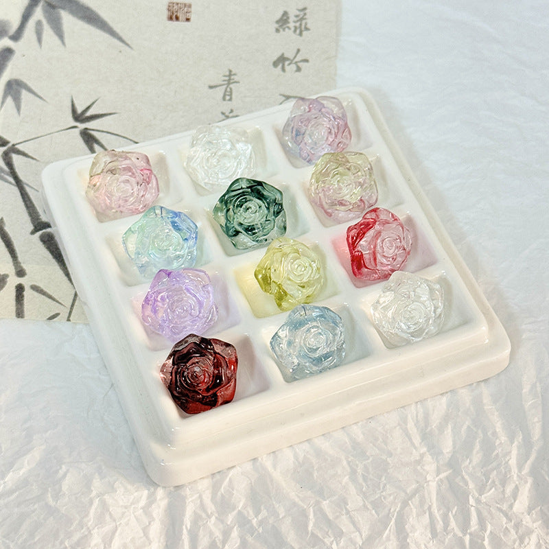 White ceramic tray holding 12 translucent rose-shaped gemstones in pastel and deep tones on a textured surface