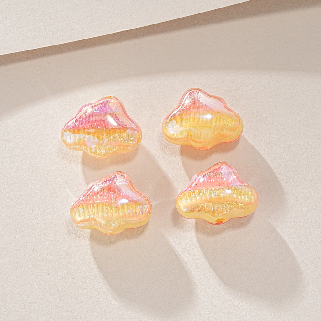 Four glossy iridescent cloud-shaped resin beads in pink, orange, and yellow on a beige surface.