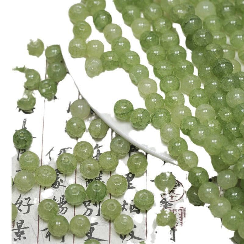 Green ice-crackle glass beads spilling from a white plate onto calligraphy paper