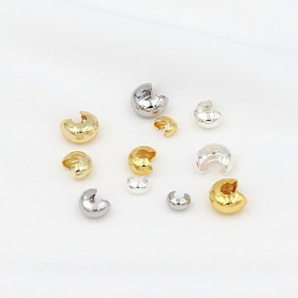 Small C-shaped crimp bead covers in polished gold and silver finishes arranged on a white background