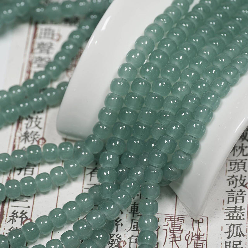 Green translucent round gemstone beads draped over a white ceramic dish on top of printed Chinese text.