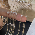 Delicate gold-plated chains with small white pearls and gold beads draped over a finger