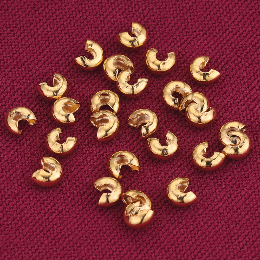Small gold C-shaped crimp bead covers scattered on dark red textured fabric.