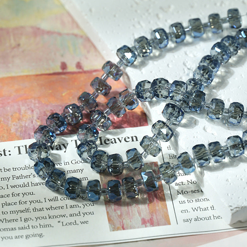 Blue faceted glass beads strung into a long necklace, arranged on top of an open book with printed text.