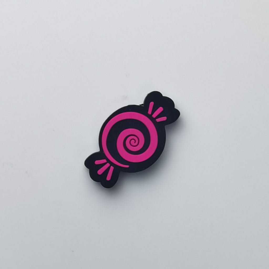 A small candy-shaped accessory with a black body and a bright pink spiral center, photographed on a plain light gray background.