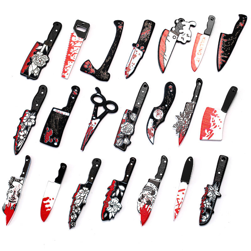 A set of 24 Halloween toy kitchen knives and utensils, including a cleaver, saw, scissors, and knives with floral and blood splatter designs, arranged in a grid on a white background.