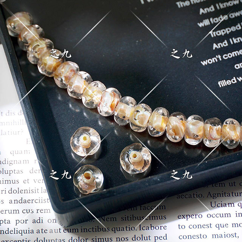 Clear lampwork glass beads with yellow-orange floral inclusions on a black tray, loose beads