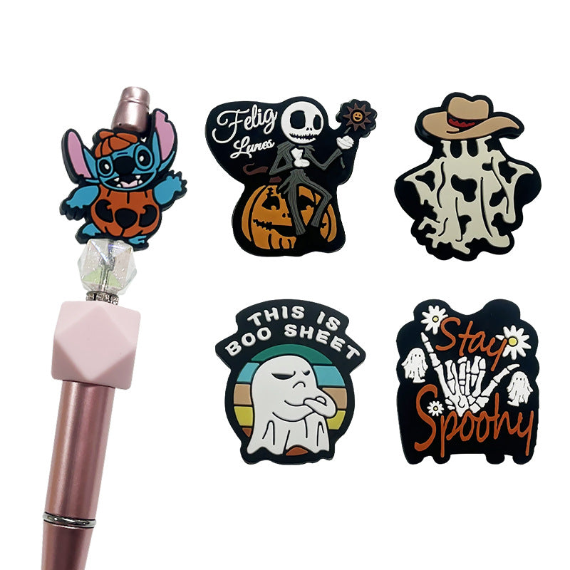 Pink pen topped with Stitch pumpkin bead beside four Halloween beads with skeleton, ghost, and skeleton-hand designs.