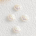 Four iridescent shell-shaped faux pearl beads on a textured white surface