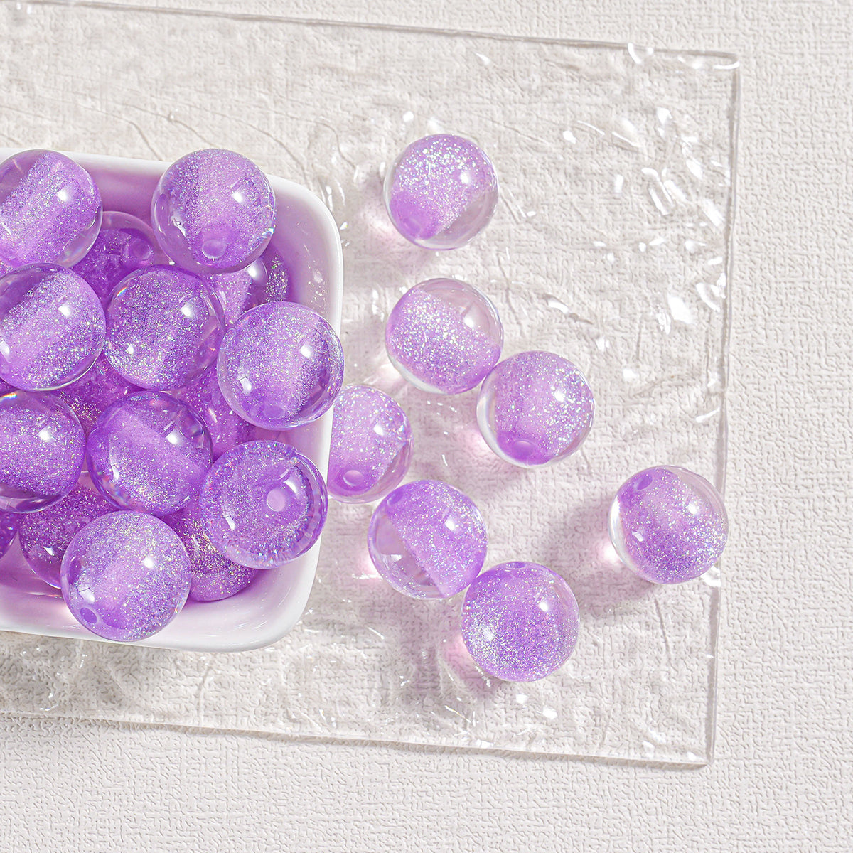 Purple glitter round beads in a white dish and scattered on a clear textured plate
