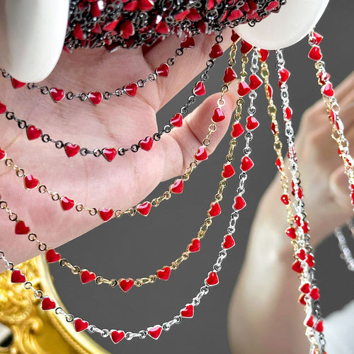 Heart-link station chains with red enamel heart charms in black, gold, and silver tones draped over a hand