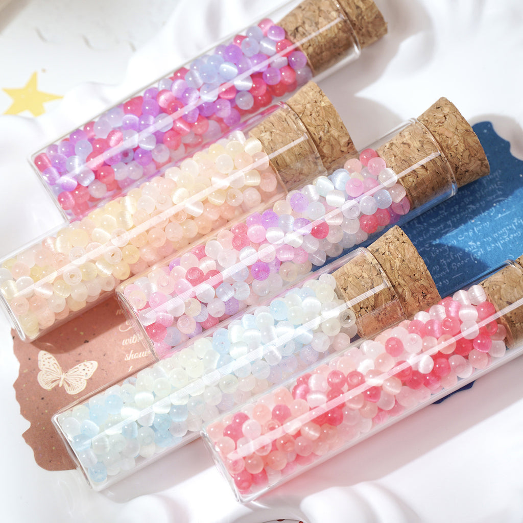 Set of decorative vials with cork lids containing colorful beads on a white background