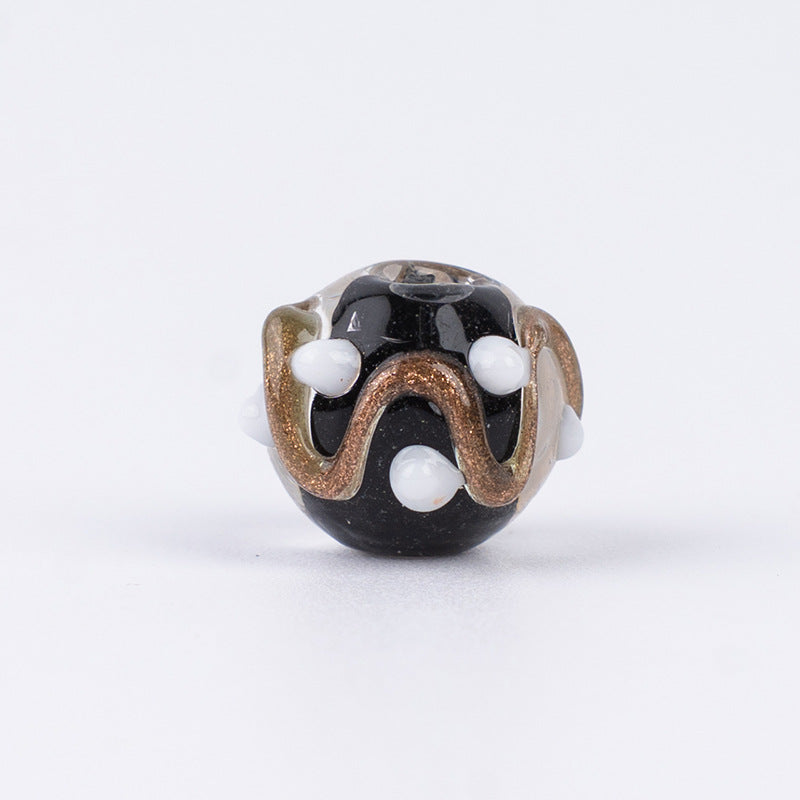 Single black gold-sand swirl glass bead with white polka dots and bronze border