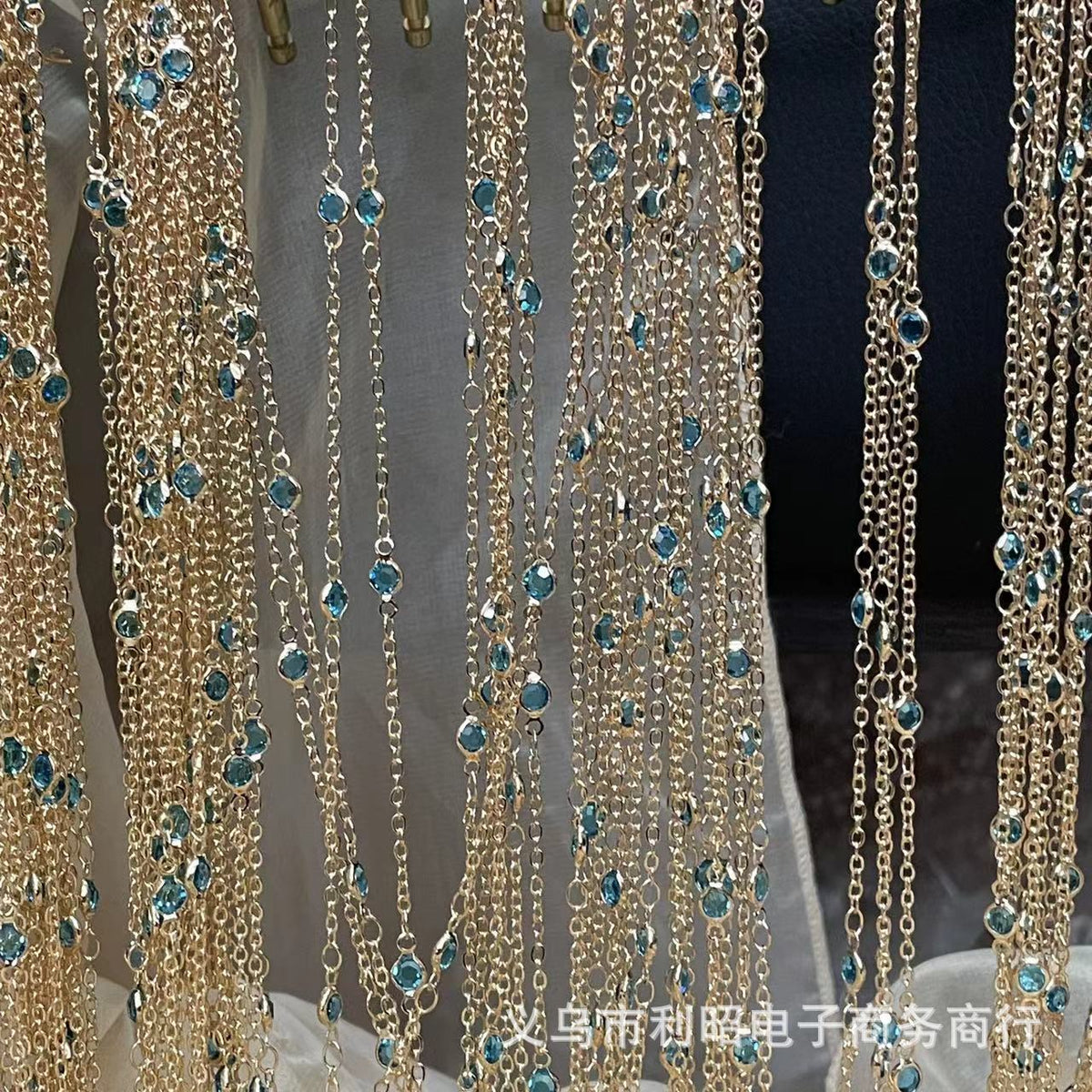 Gold-tone beaded chain curtains with small faceted blue-green rhinestones hanging in multiple strands against a dark background.