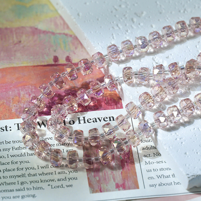 Strand of faceted pink glass beads with iridescent finish draped across a colorful magazine page and textured white surface