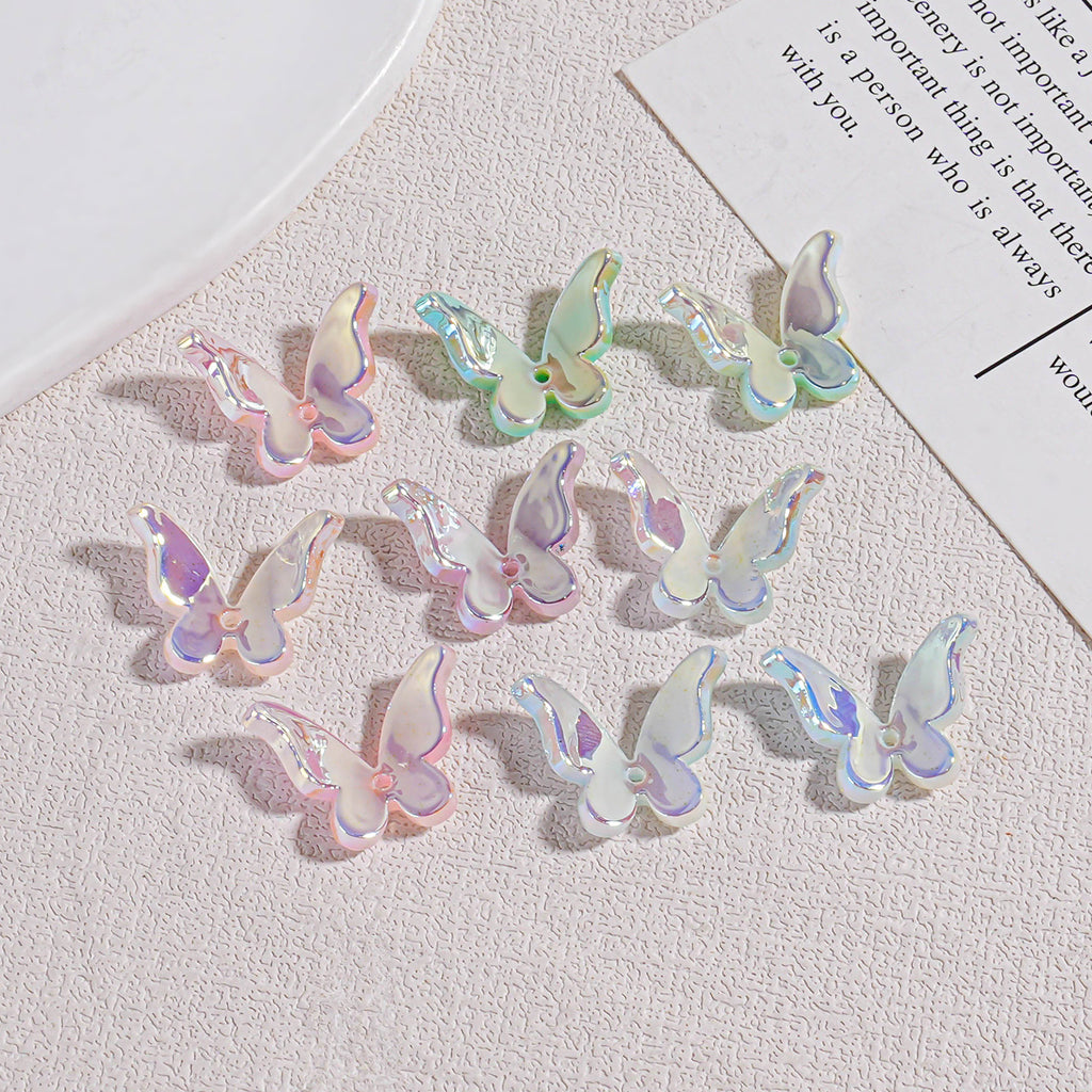 Twelve iridescent butterfly acrylic beads on textured beige surface with plate and paper