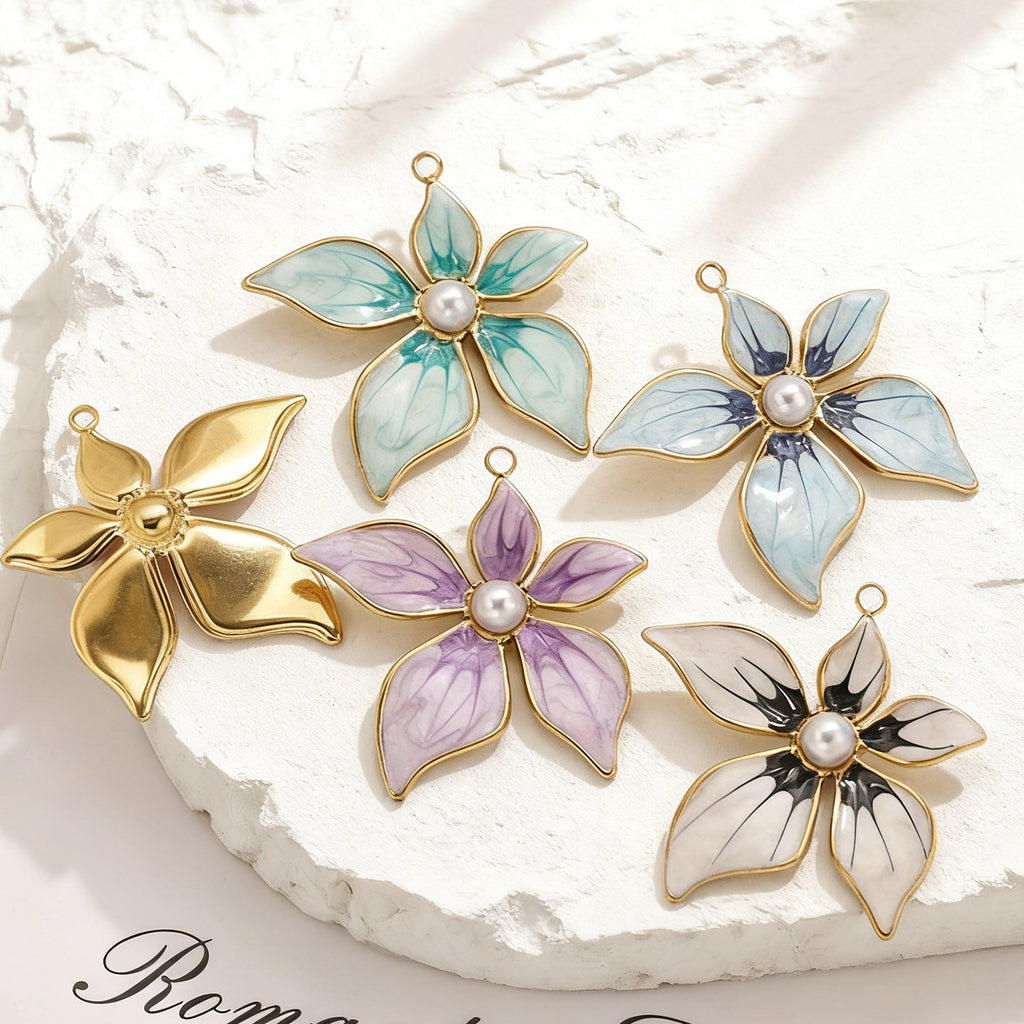 Five gold-toned flower pendant charms, four with enamel petals and pearl centers, on a white stone surface