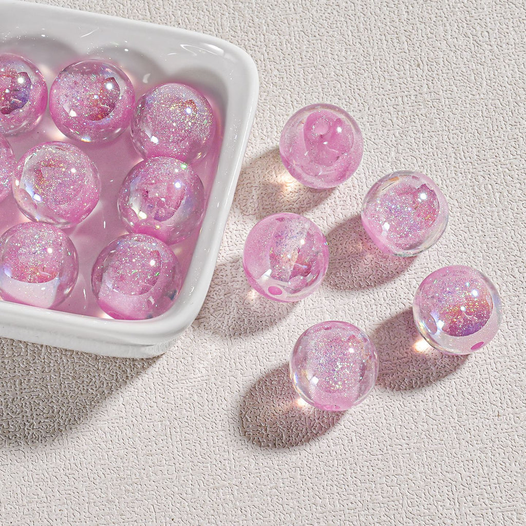 Pink glitter-filled candy-core opal-effect resin round beads in white dish on textured beige surface