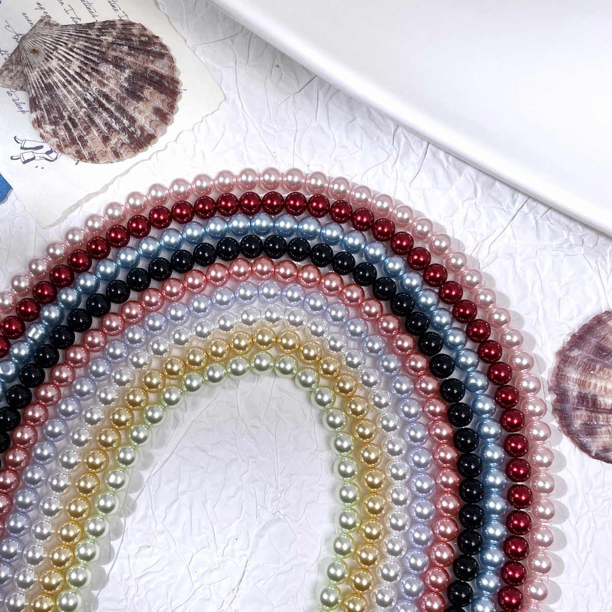 Concentric arcs of glass pearl bead strands in pink, red, blue, black, and gold with seashell props