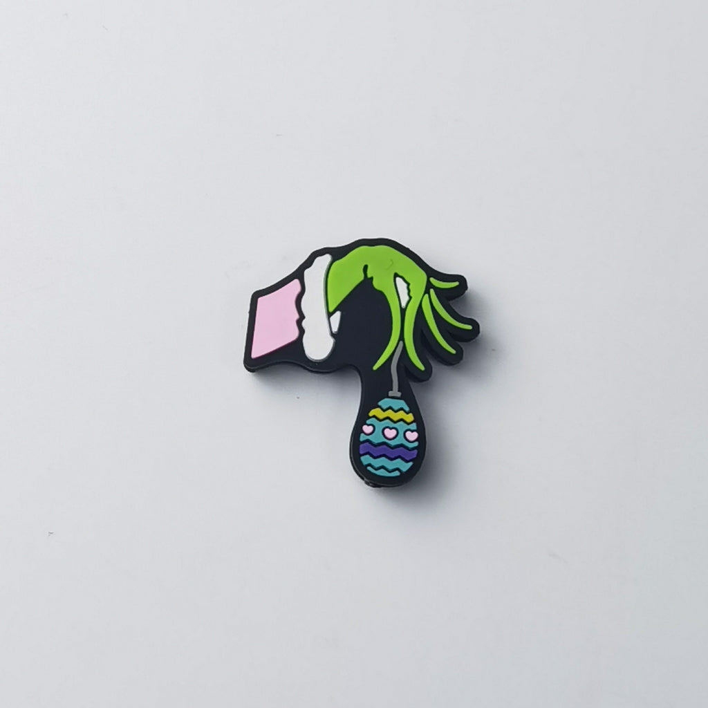 Green Grinch hand silicone focal bead in pink-and-white striped sleeve, holding patterned blue and yellow ornament