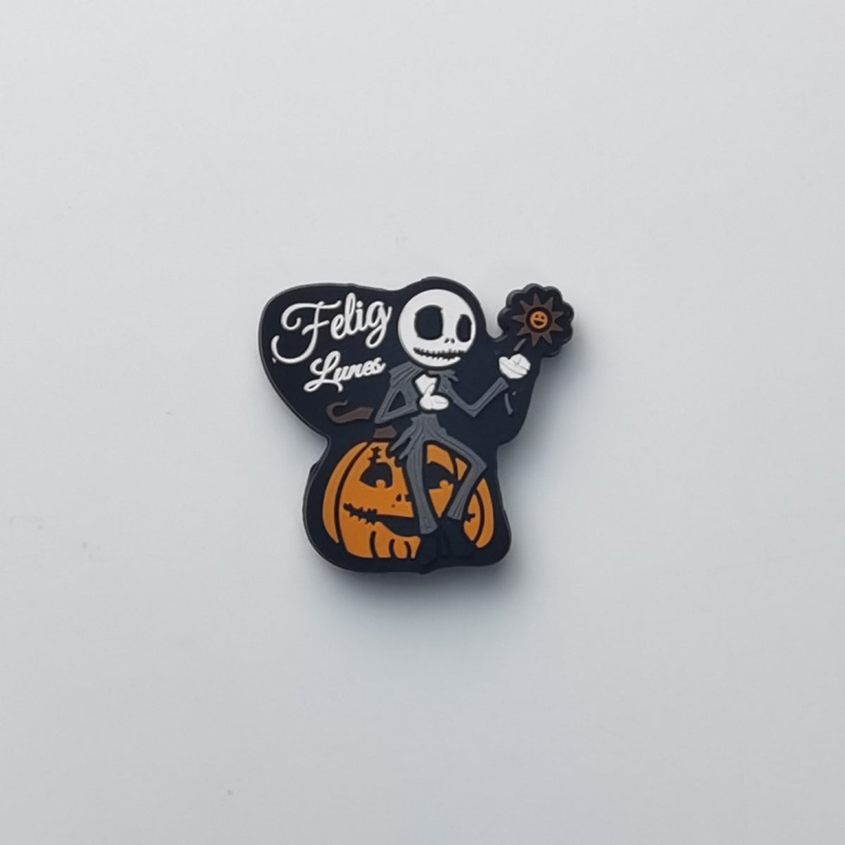 A small Halloween-themed enamel pin featuring Jack Skellington sitting on a carved pumpkin, with a black shape behind him that reads 'Felicity Lancer' in white script. The pin is photographed on a plain light gray background.