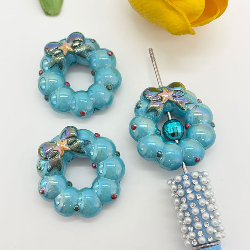 Two wreath-shaped acrylic focal beads that look like beaded hoops on a white background
