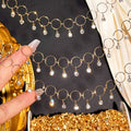 Gold chain necklace with circular links and dangling clear crystal charms, shown draped across a dark surface with a hand holding a section and a gold jewelry box visible.