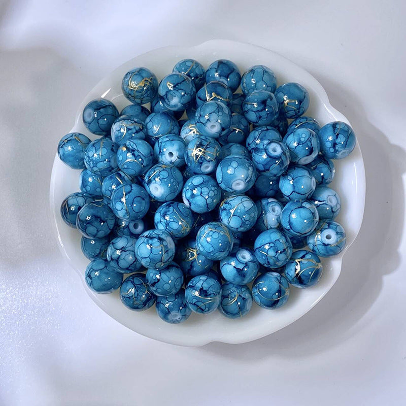 White bowl of marbled teal-blue glass beads with gold-silk veining