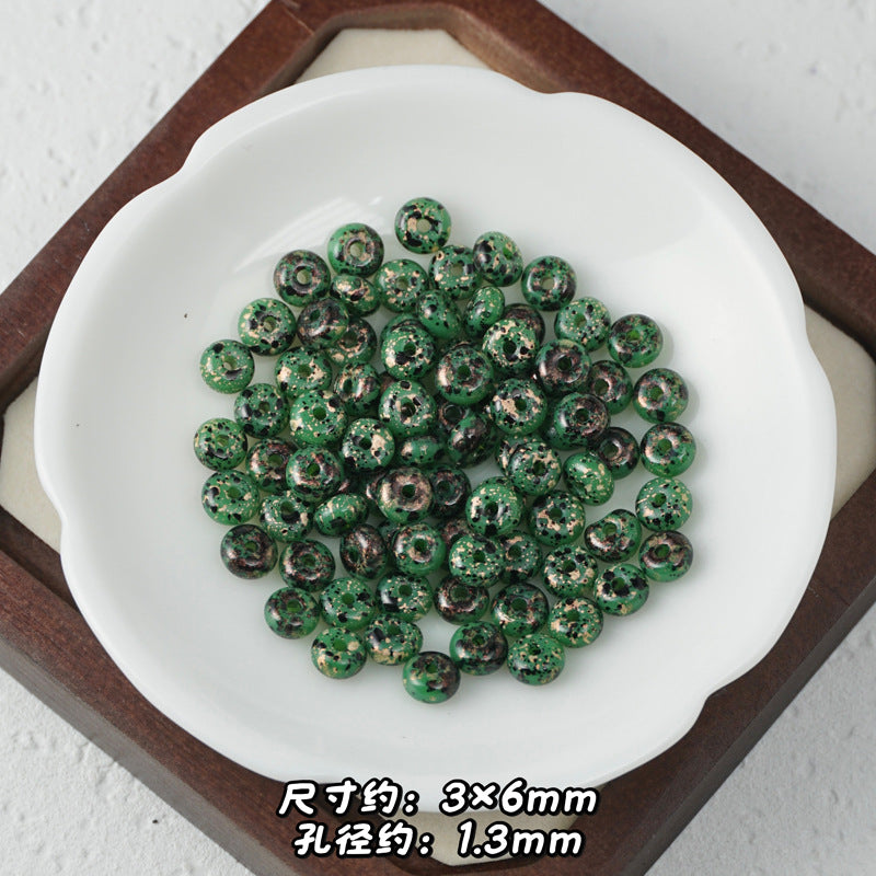 Green marbled Picasso glass abacus beads with gold glitter accents in a white ceramic dish.