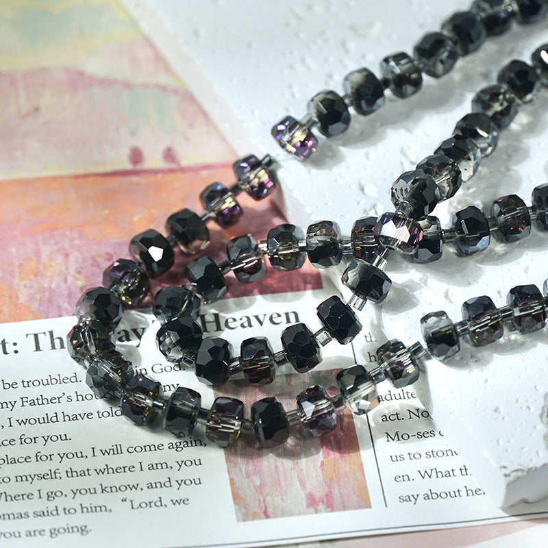 Faceted black glass beads with a smoky gray finish arranged in loops over printed text on a white textured surface