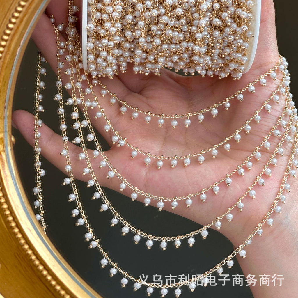 Hand holding gold 3mm white glass pearl fringe chain strands over palm, gold mirror behind.