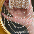 Hand holding gold 3mm white glass pearl fringe chain strands over palm, gold mirror behind.