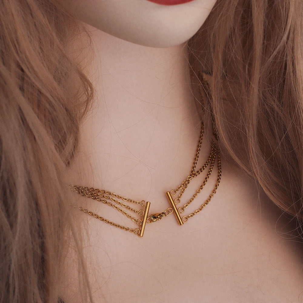 A close-up of a model's neck and lower face wearing a gold multi-strand chain necklace with two vertical bar charms.