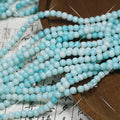 Multiple strands of light blue and white round porcelain beads on wooden surface
