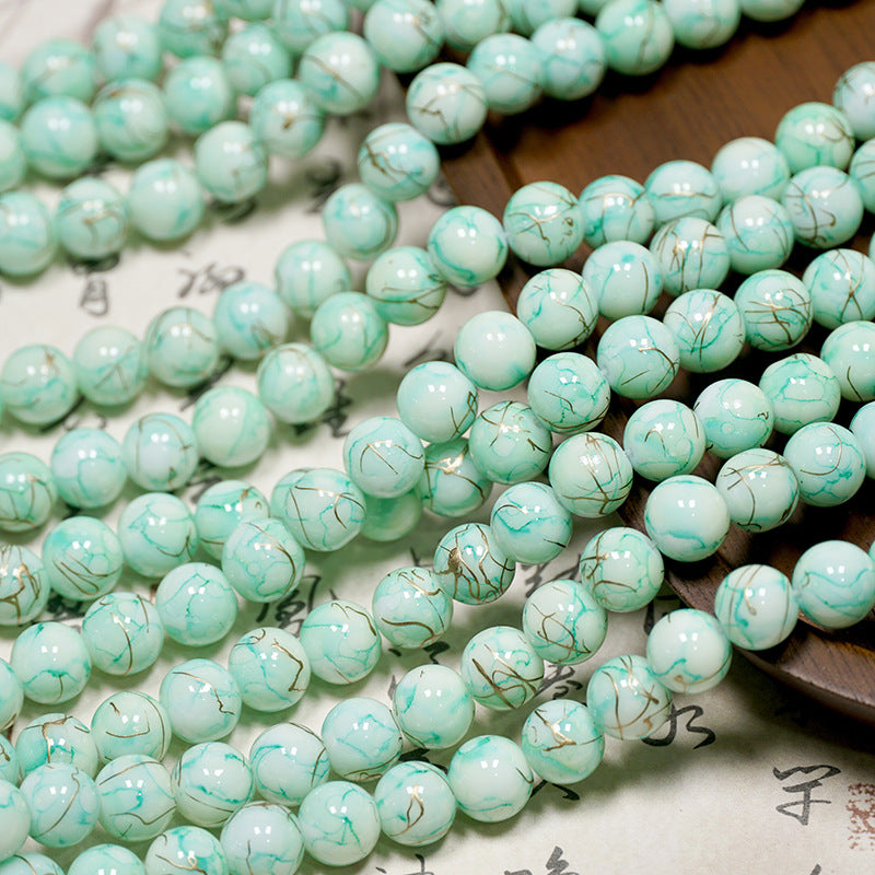 Close-up of pale mint-green porcelain beads with gold veining on a light surface