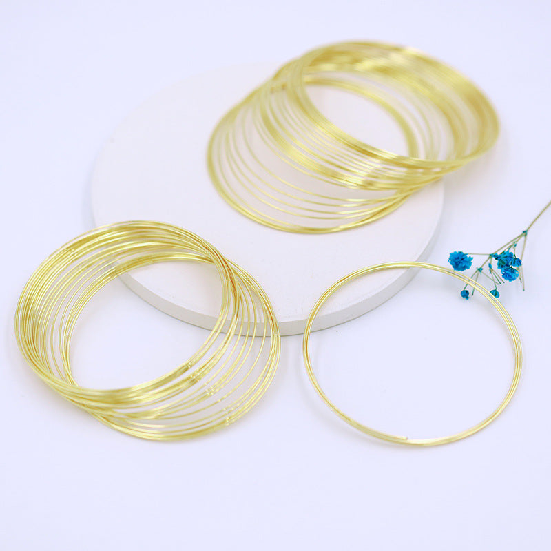 Gold-plated memory wire bracelet rings arranged around white display platform with blue flowers