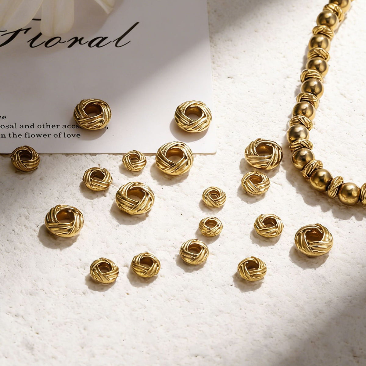 Gold-tone twisted bird's nest beads and a beaded bracelet on a textured white surface