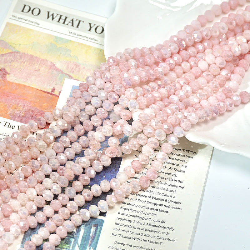 Strands of faceted light pink porcelain beads on printed papers and a white dish
